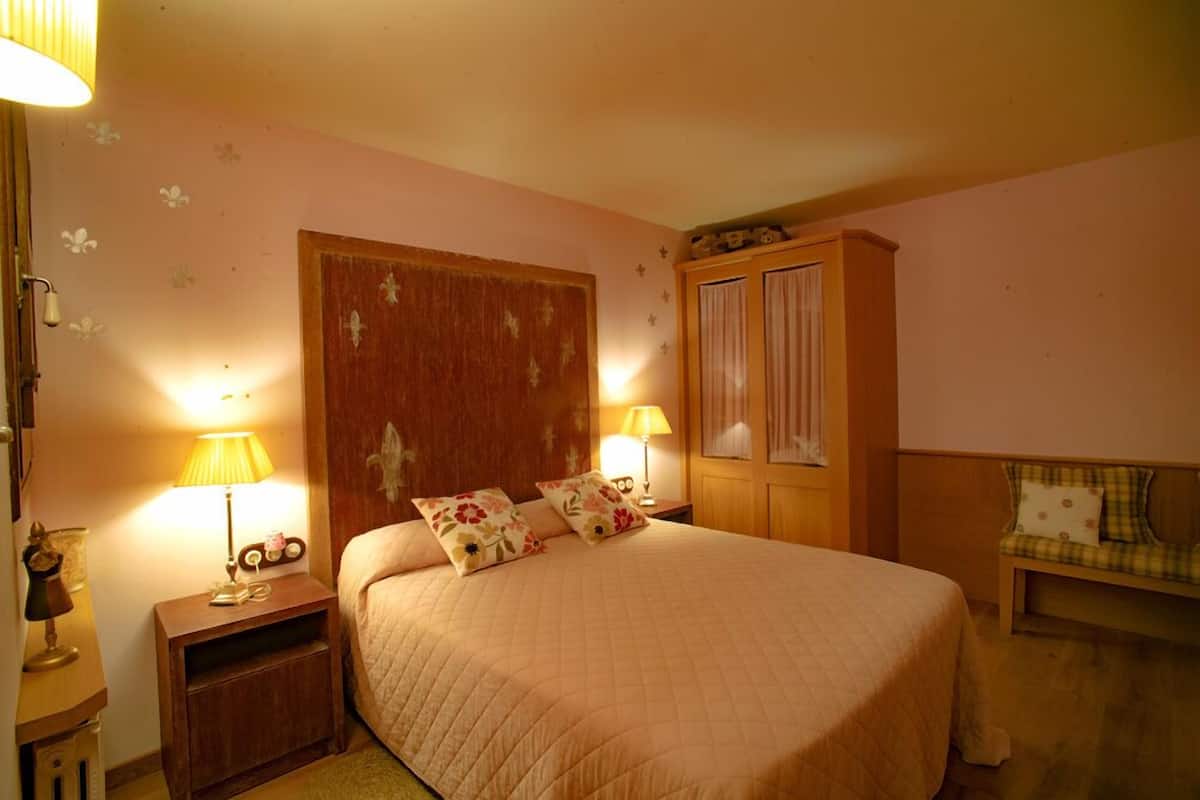 Une chambre à coucher avec un grand lit, deux lampes de chevet, une armoire en bois et un banc avec un coussin.