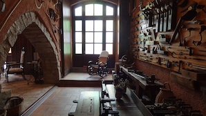 Un intérieur rustique avec une arche en pierre, un banc en bois et divers outils exposés au mur.