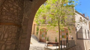 Un couloir voûté en pierre, avec un plafond en bois, qui mène à un bâtiment doté d’un escalier et d’un banc.