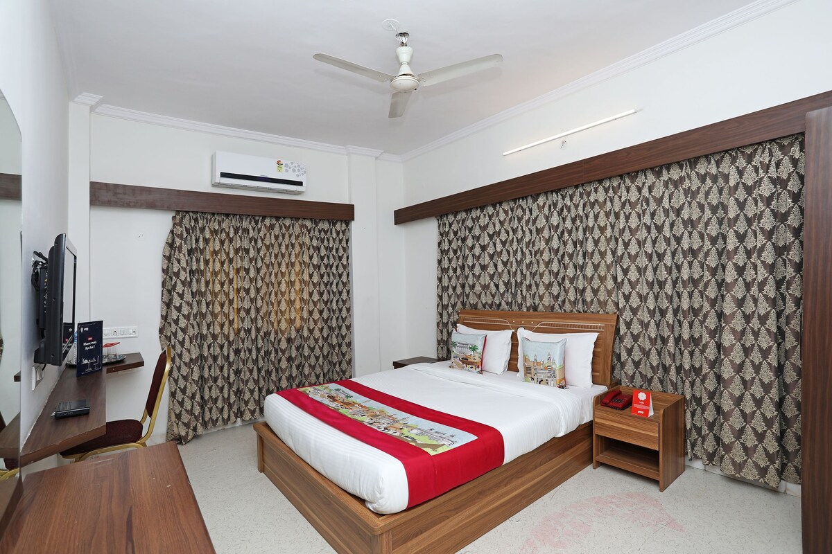 A hotel room with a bed, a desk, a chair, a nightstand, and a ceiling fan.