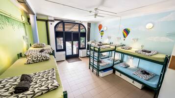 Una habitación con literas, ventilador de techo y vistas por una puerta.