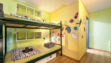 Un lit superposé avec une structure verte et un lit inférieur recouvert d’une couverture à motifs. La pièce a un mur jaune orné d’autocollants représentant des chats de dessins animés.