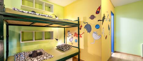 Cama litera con estructura verde y una cama inferior cubierta con un edredón estampado. La habitación tiene una pared amarilla decorada con pegatinas de gatos de dibujos animados.