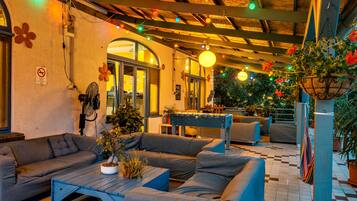 An outdoor seating area with sofas and a table, surrounded by potted plants and string lights.
