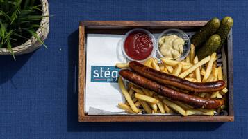 Una bandeja con salchichas, papas fritas y salsas sobre una superficie azul.