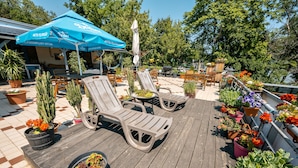 A wooden deck with lounge chairs, potted plants, and a blue umbrella. - Island Hostel - Adults only (Budapest)