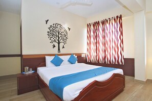 Una cama bien hecha con ropa de cama azul y blanca, un cabecero de madera y una decoración en la pared con un árbol y pájaros.