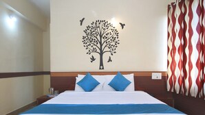 Una habitación de hotel con una cama, un mural en la pared con un árbol y pájaros, y una cortina estampada.
