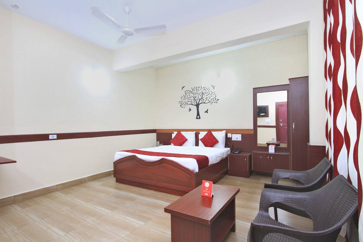 A hotel room with a wooden bed, a nightstand, a desk, and two chairs.