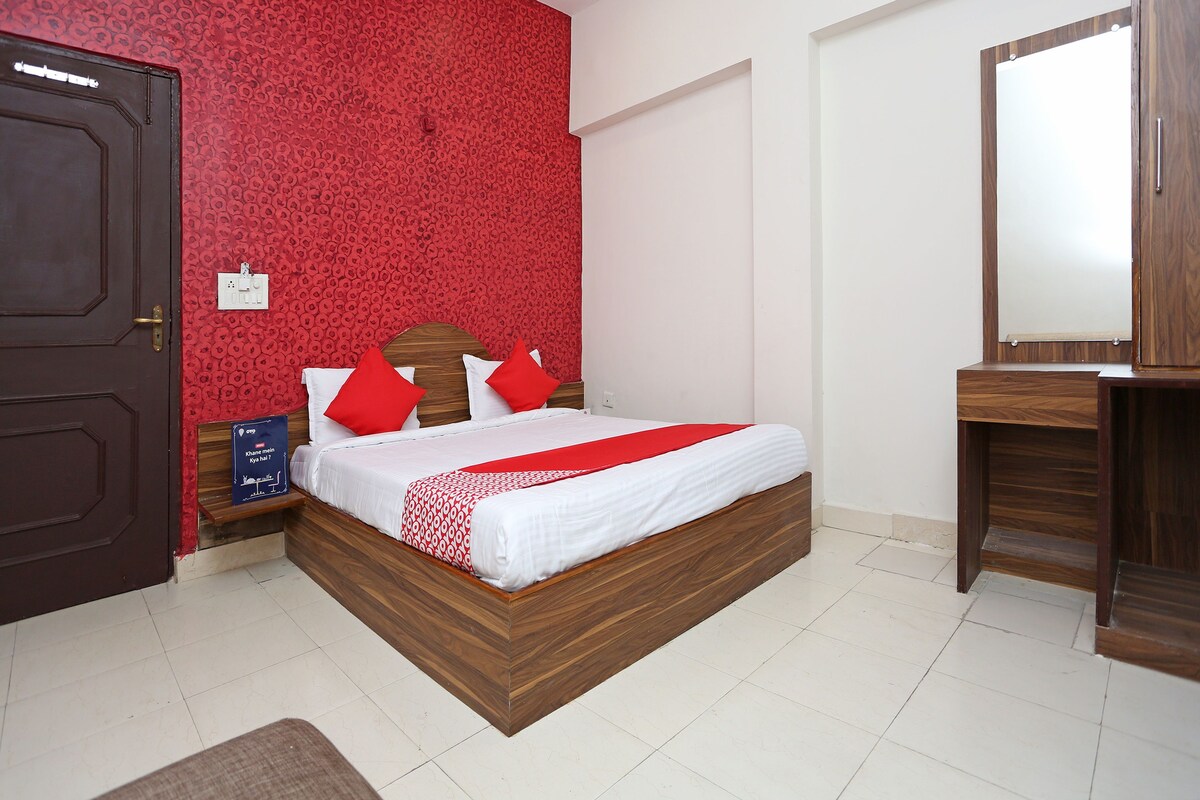 A bedroom with a wooden bed, red patterned wallpaper, a white bedside table, and a mirror.