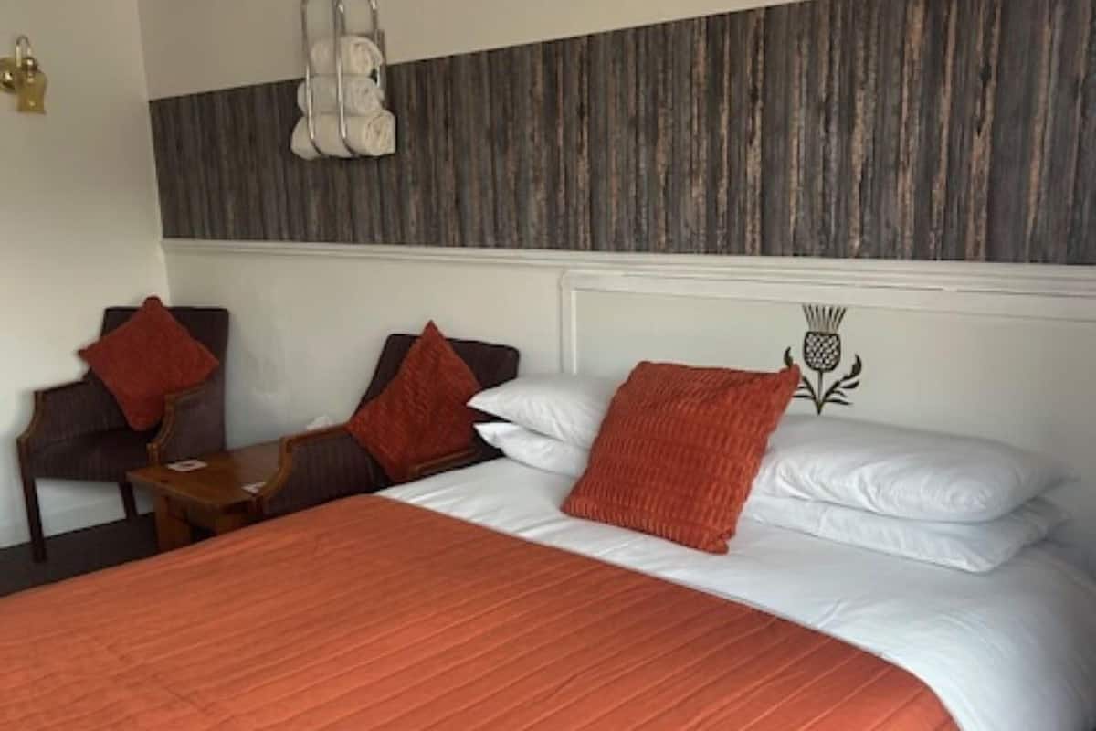 Una camera d'albergo con un letto grande, una testiera in legno, un tavolino e una sedia.