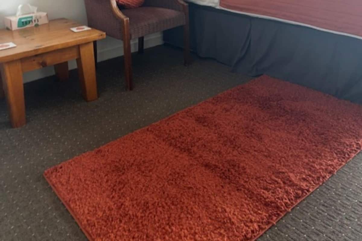 Una camera d'albergo con un letto, una sedia, un tavolino e un tappeto rosso.