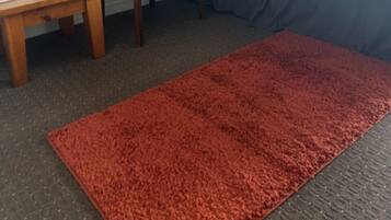 Une chambre d’hôtel avec un lit, une chaise, une petite table et un tapis rouge.