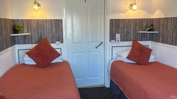 Una habitación de hotel con dos camas, una puerta, una alfombra pequeña y luces fijadas en la pared.
