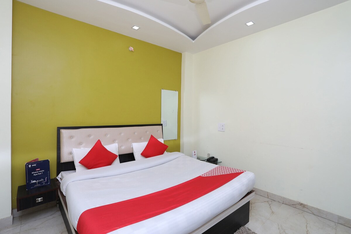A hotel room with a bed, a nightstand, a red and white bedspread, and a yellow accent wall.