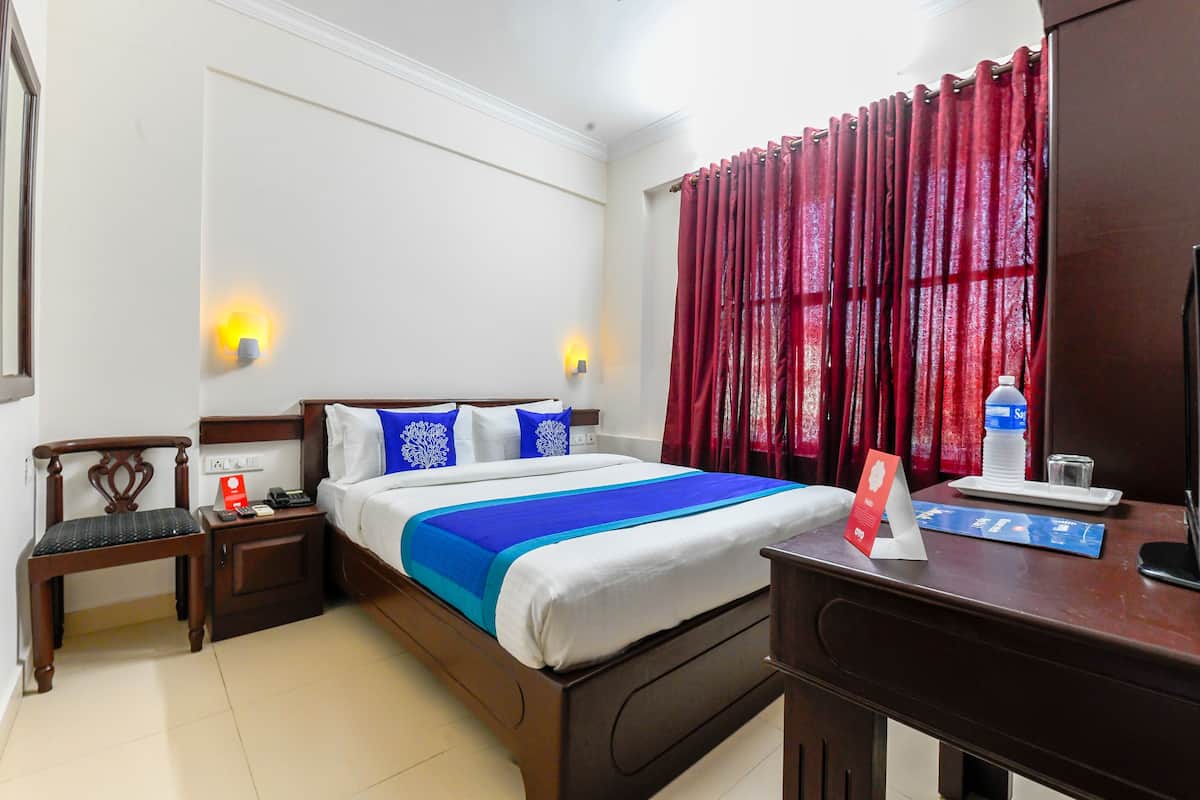 A hotel room with a bed, a nightstand, a chair, a desk, a TV, and a window with curtains.