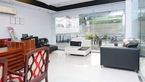 A modern hotel lobby with a reception desk, seating area, and large windows offering a view of the outdoors. - Capital O 10611 Hotel Malabar Illam (Kanayannur)