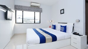 A modern bedroom with a large bed, a bedside table, a TV mounted on the wall, and a window with a view of buildings. - Capital O 10611 Hotel Malabar Illam (Kanayannur)