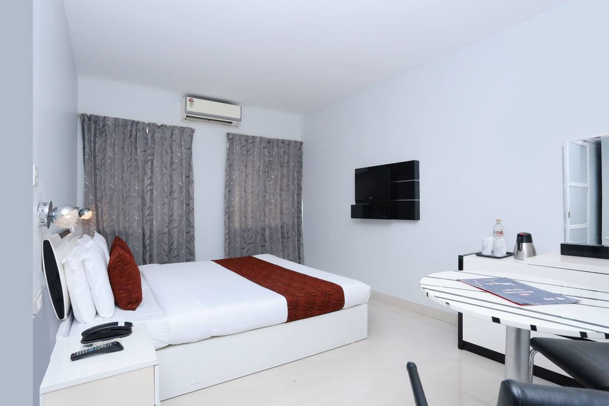 A modern hotel room with a bed, bedside table, and a desk with a chair.