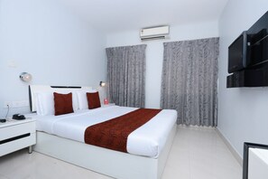 A hotel room with a bed, a bedside table, a TV, and an air conditioning unit. - Capital O 10611 Hotel Malabar Illam (Kanayannur)