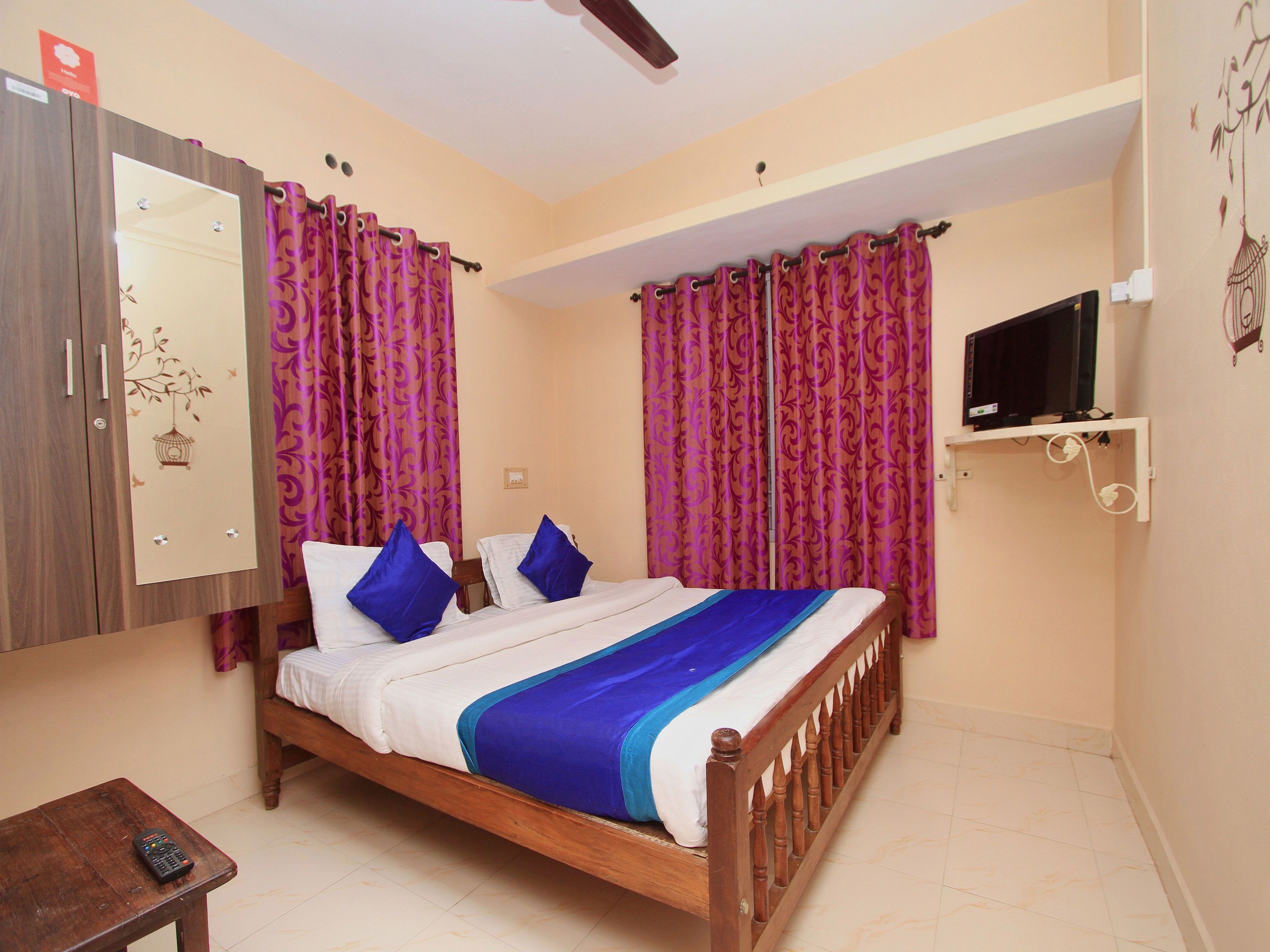 A bedroom with a wooden bed, purple curtains, a TV on a shelf, and a wardrobe with a mirror.