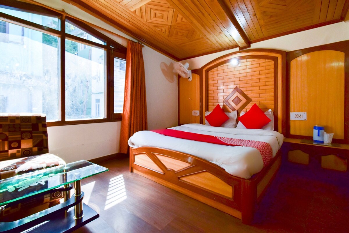 A hotel room with a wooden ceiling, a large bed with red and white bedding, a glass coffee table, and a brick wall.