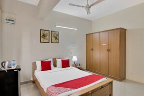 Habitación de hotel con cama, armario, escritorio con tetera y ventilador de techo.