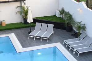 Una piscina al aire libre, sombrillas, sillones reclinables de piscina