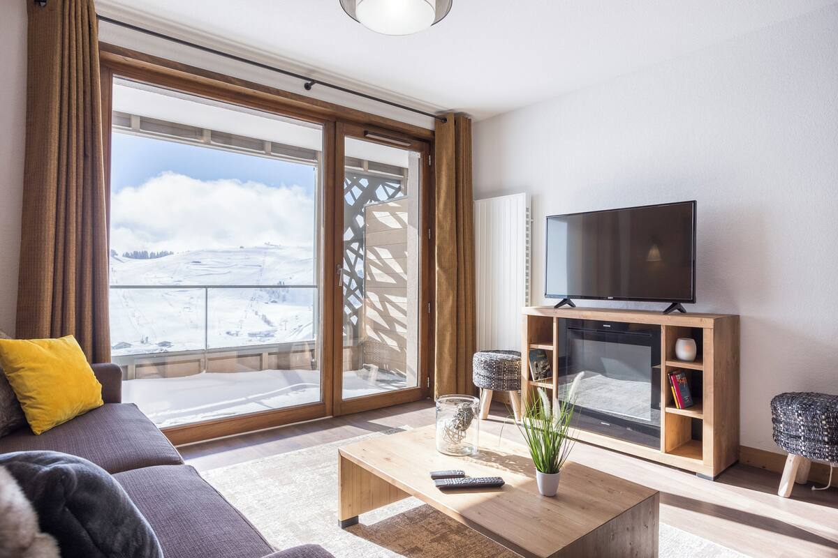 Un salon moderne doté d’une grande porte-fenêtre coulissante donnant sur un balcon, d’un téléviseur à écran plat et d’un coin salon confortable.