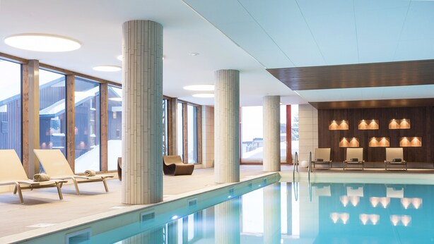 Ein moderner, überdachter Pool mit klarem Wasser, Liegestühlen und großen Fenstern.