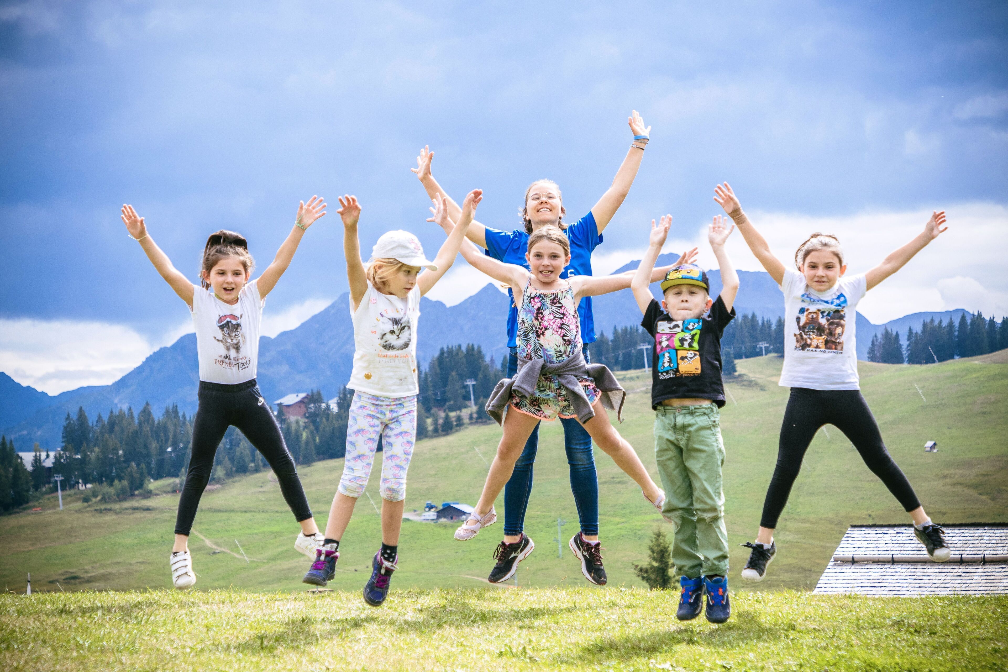 A group of people jumping on a grassy field with mountains in the background.