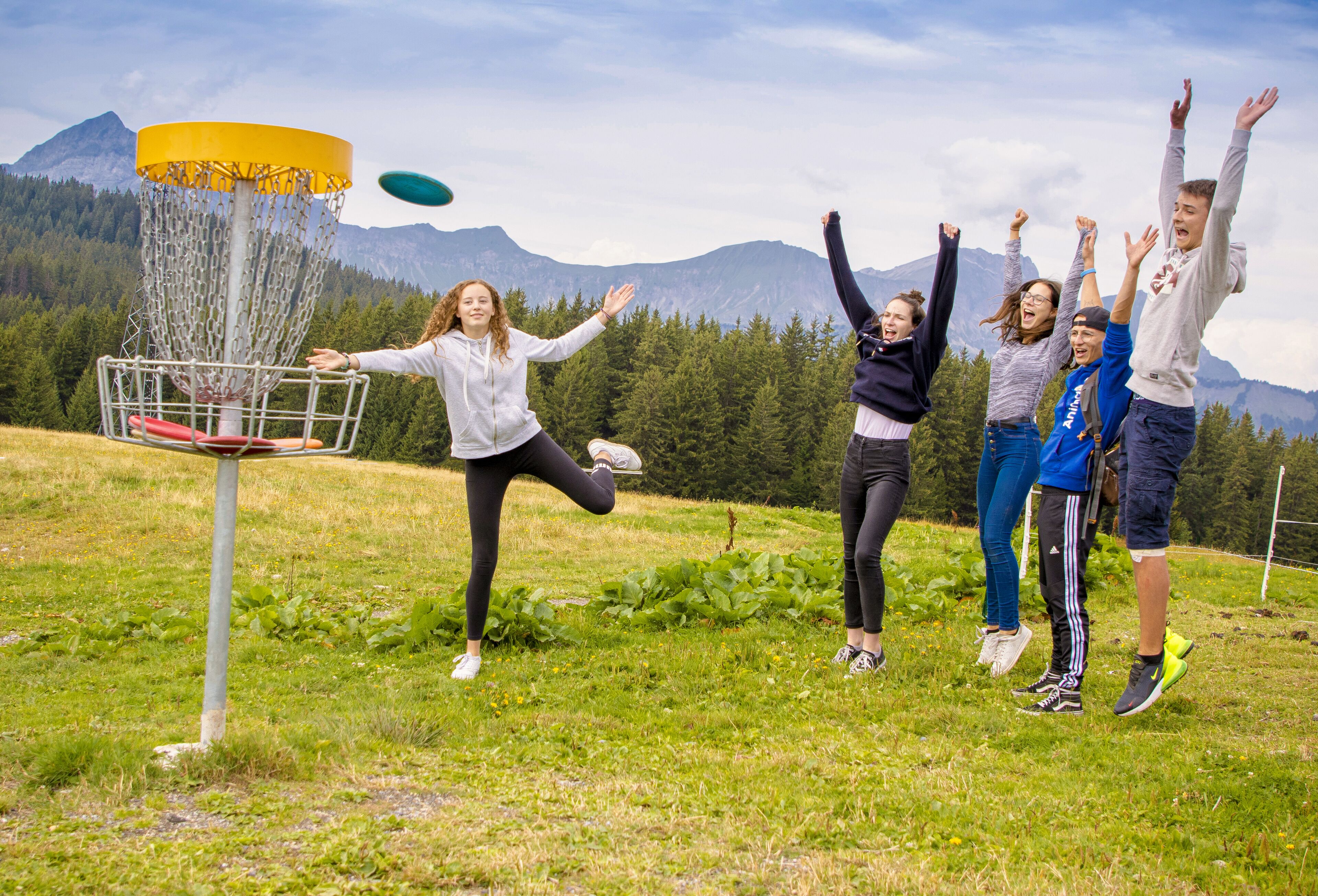 A group of people playing frisbee in an outdoor setting with a mountain backdrop.
