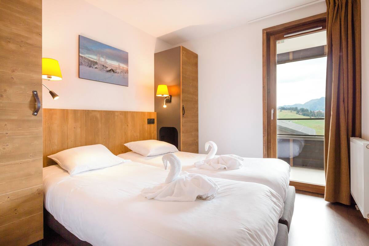 Hotelkamer met twee bedden, een houten hoofdbord, een schilderij aan de muur en uitzicht op een landschap door het raam.