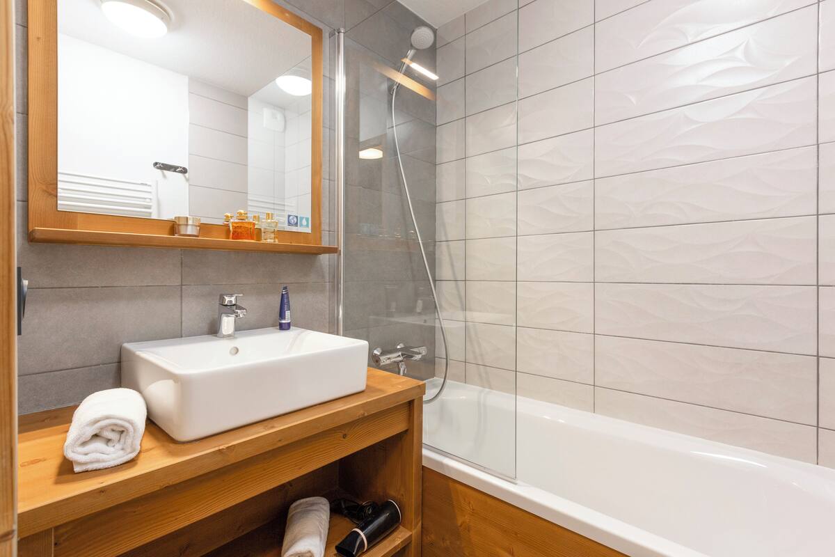 Une salle de bain avec un lavabo blanc, un meuble-lavabo en bois, un miroir et une douche à parois de verre.