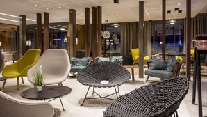 Ein stilvoller Lounge-Bereich mit verschiedenen Sitzmöglichkeiten, darunter ein Korbstuhl, ein gelber Sessel und ein graues Sofa.