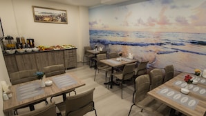 A dining area with tables set for four, a kitchen counter with various items, and a large beach mural on the wall.
