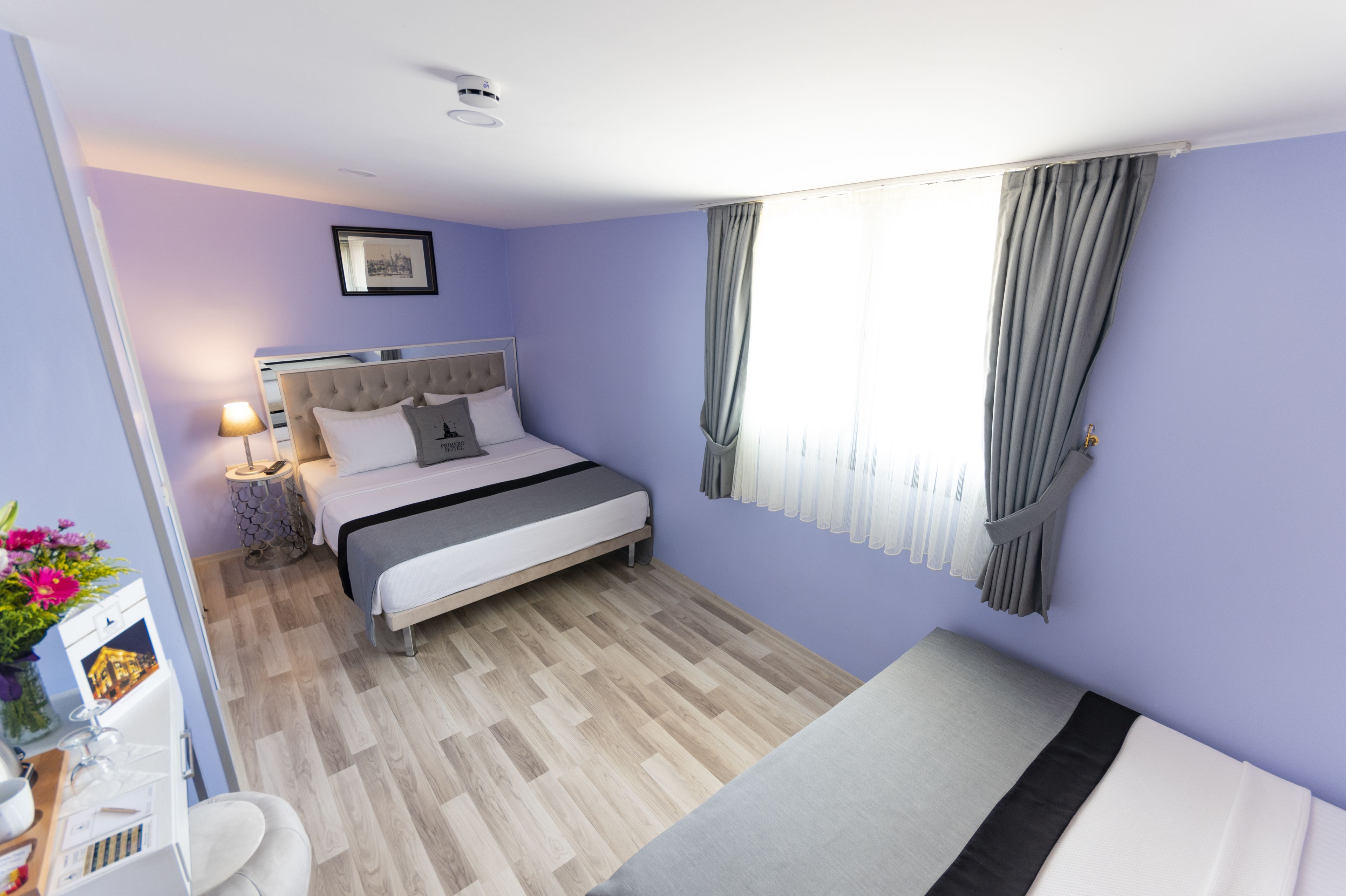 Una camera d'albergo moderna con un letto, un comodino, una lampada e una finestra con tende.