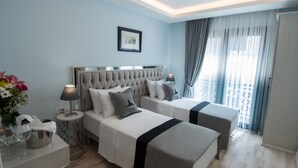 A hotel room with two beds, a bedside table with a lamp, a framed picture on the wall, and a window with curtains.