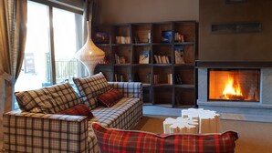 A cozy living room with a fireplace, a sofa set, and a bookshelf. - Résidence MMV La Clé des Cimes (Beaufort)