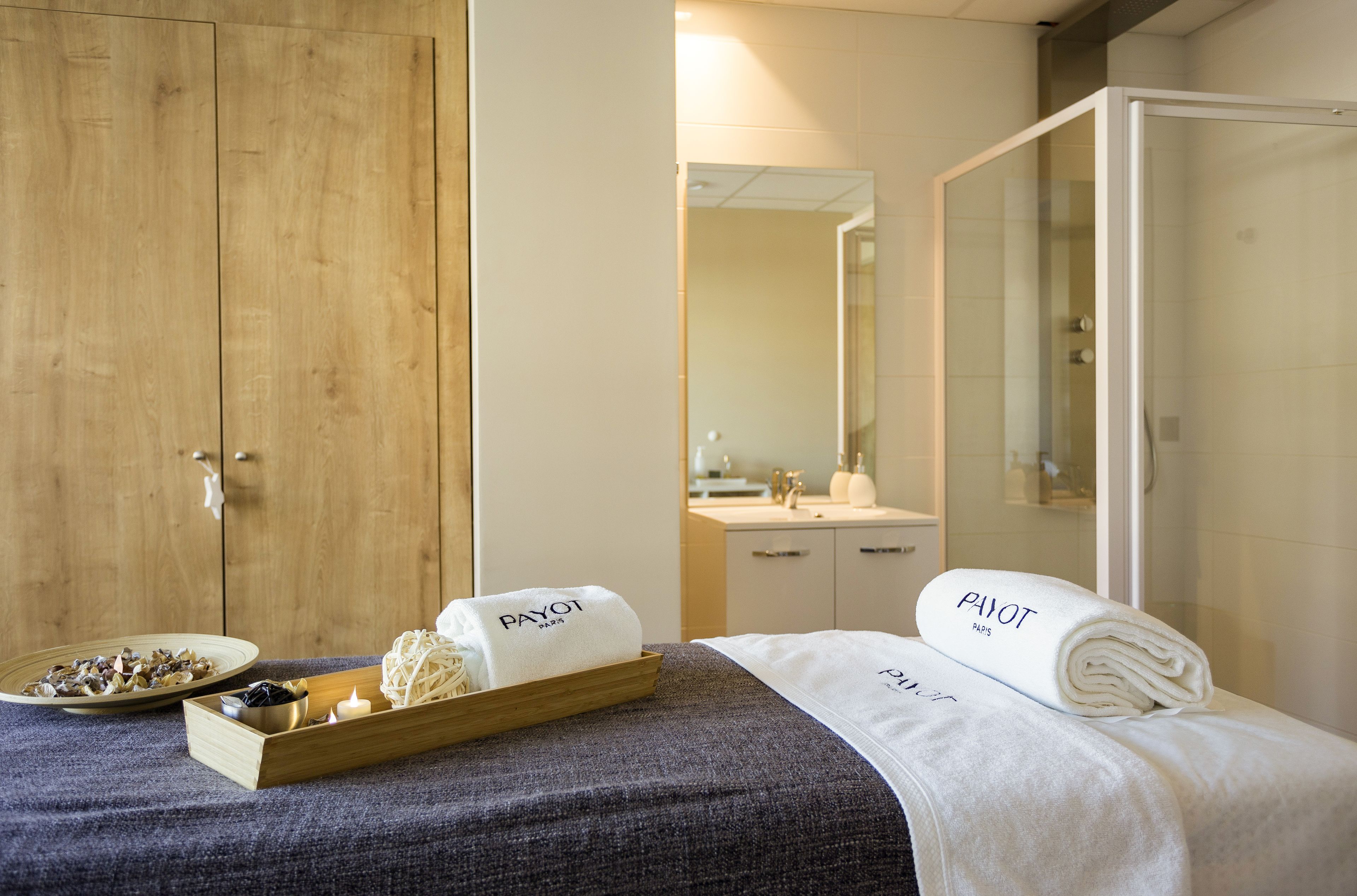 A hotel room with a wooden wardrobe, a bed with a white towel, a tray with candles and a small bowl, and a mirror on the wall.