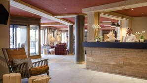 A reception area with a wooden reception desk, a bench with plaid cushions, and a large pillar. - Résidence MMV La Clé des Cimes (Beaufort)