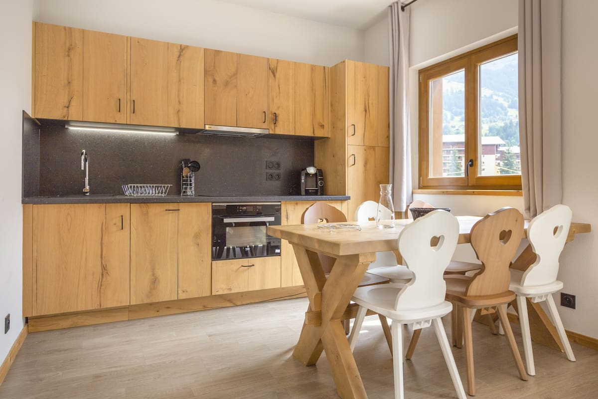 Een moderne keuken met houten kastjes, een zwart aanrecht en een eethoek met witte stoelen.