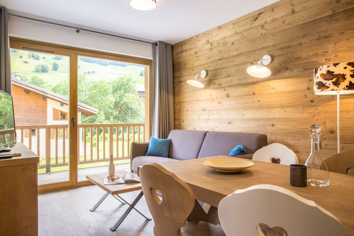 Een houten interieur met een bank, eettafel, stoelen en uitzicht door een glazen deur.