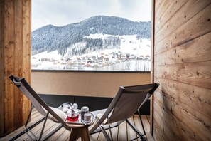 Un balcon en bois avec deux chaises et une table, donnant sur un village de montagne enneigé.