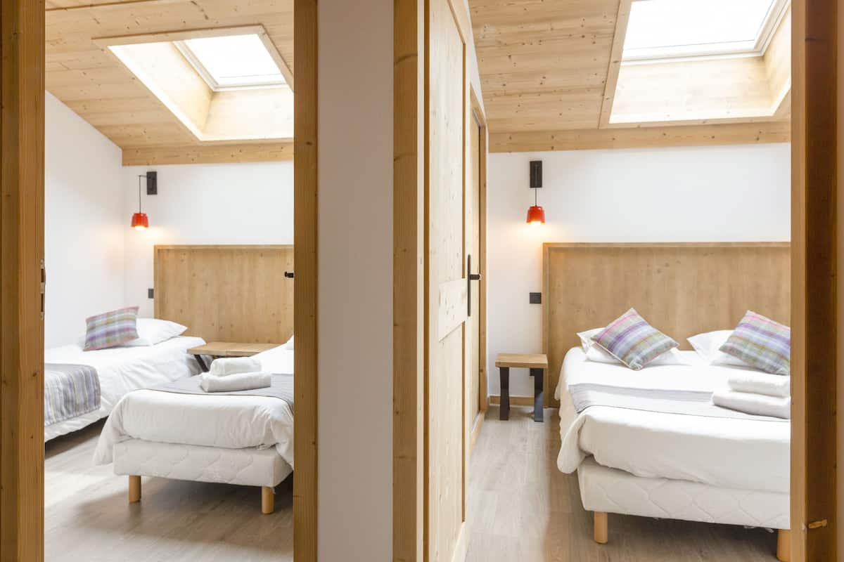 Een slaapkamer met twee bedden, houten balken, een dakraam en een klein tafeltje.