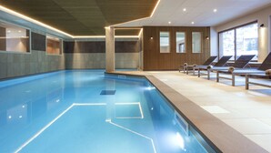 A modern indoor swimming pool with clear water, lounge chairs, and a wooden panel wall with windows. - Résidence MMV La Clé des Cimes (Beaufort)