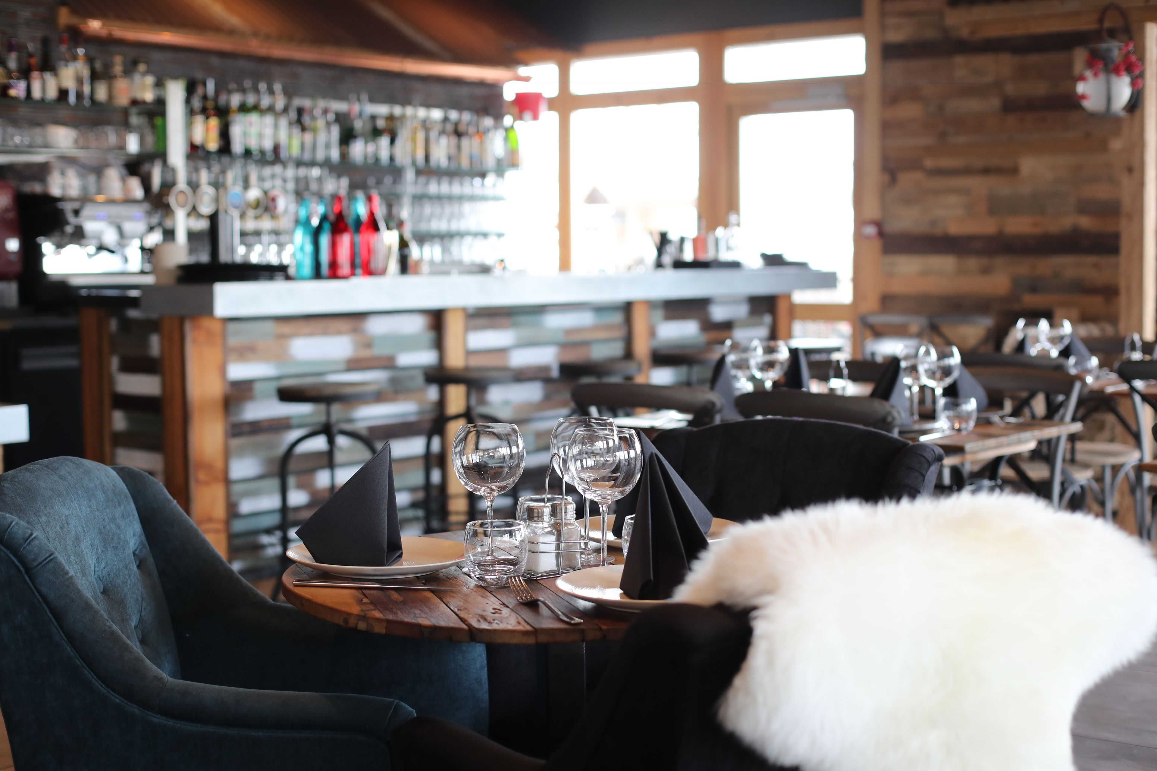 A restaurant with wooden tables, chairs, and a bar area with various bottles.
