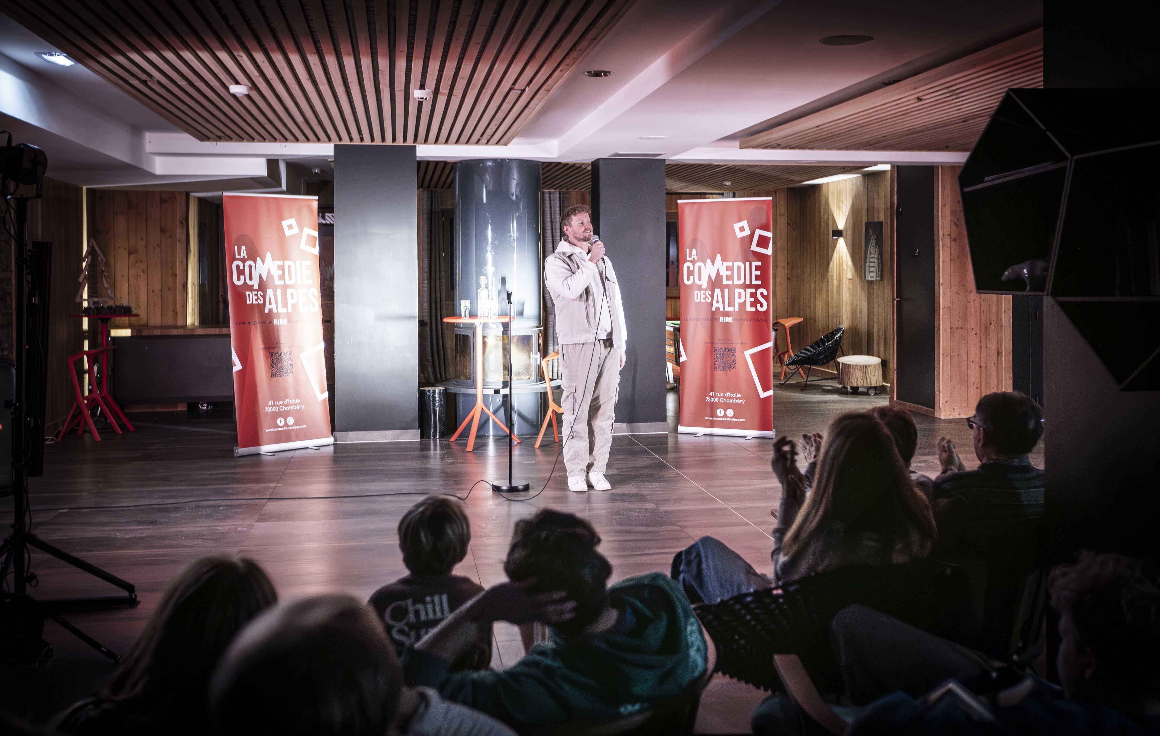 A stage with a speaker and an audience in a modern interior with wooden accents and a high ceiling.