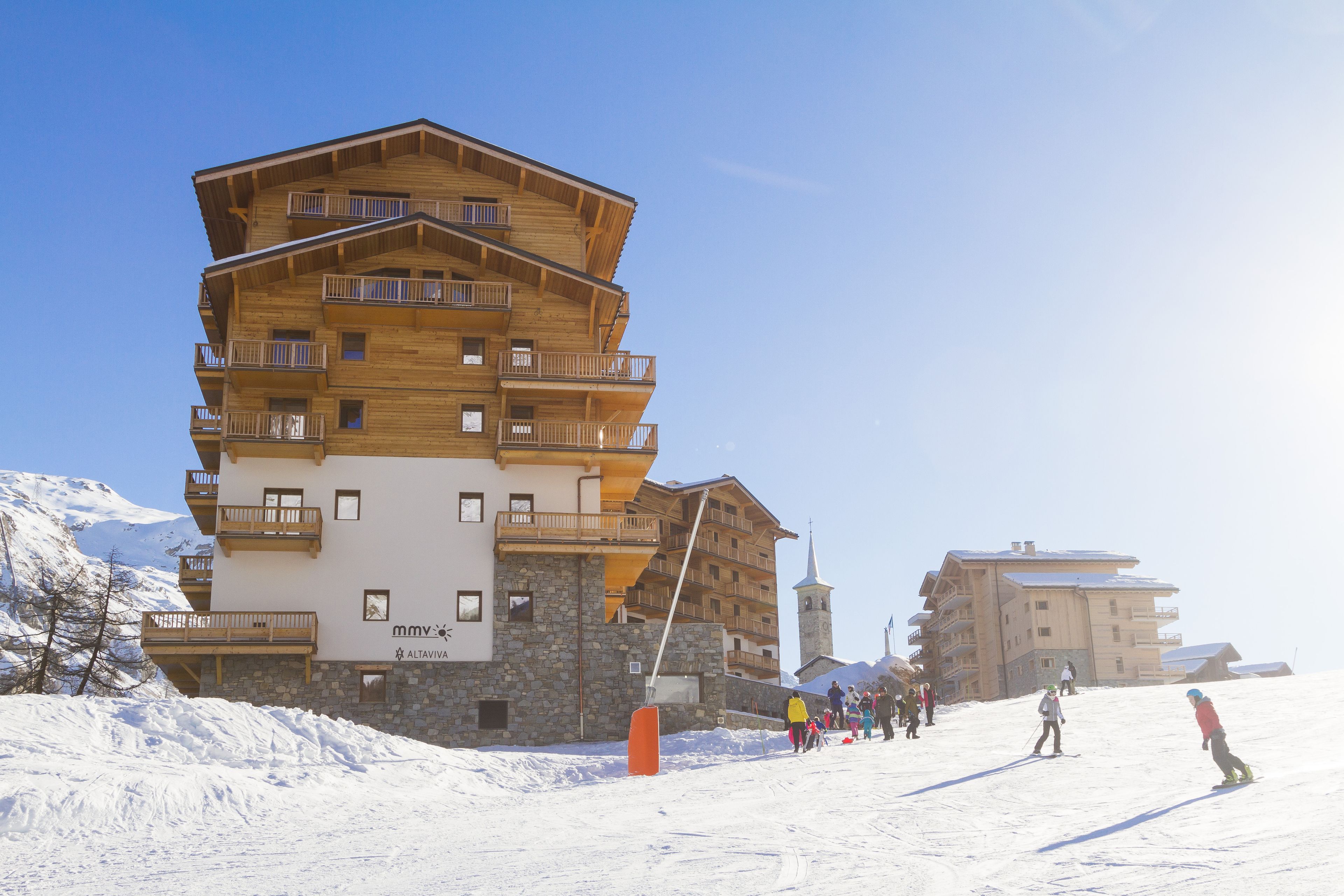 A multi-story wooden building with balconies, ski slopes, and a mountainous backdrop.
