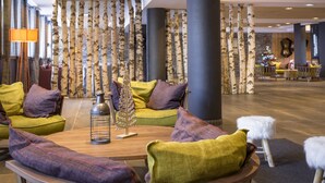 A lobby with a wooden coffee table, green and purple sofas, a decorative tree, and a Christmas tree in the background. - Résidence Club MMV l'Altaviva (Tignes)